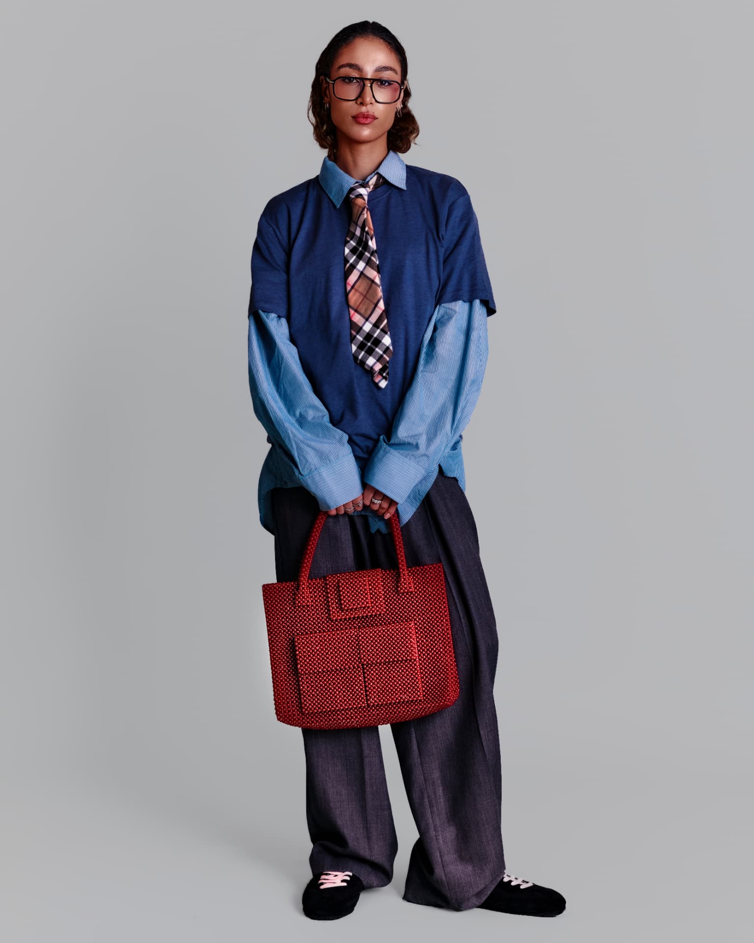 Model in layered blue shirting holding a red beaded tote