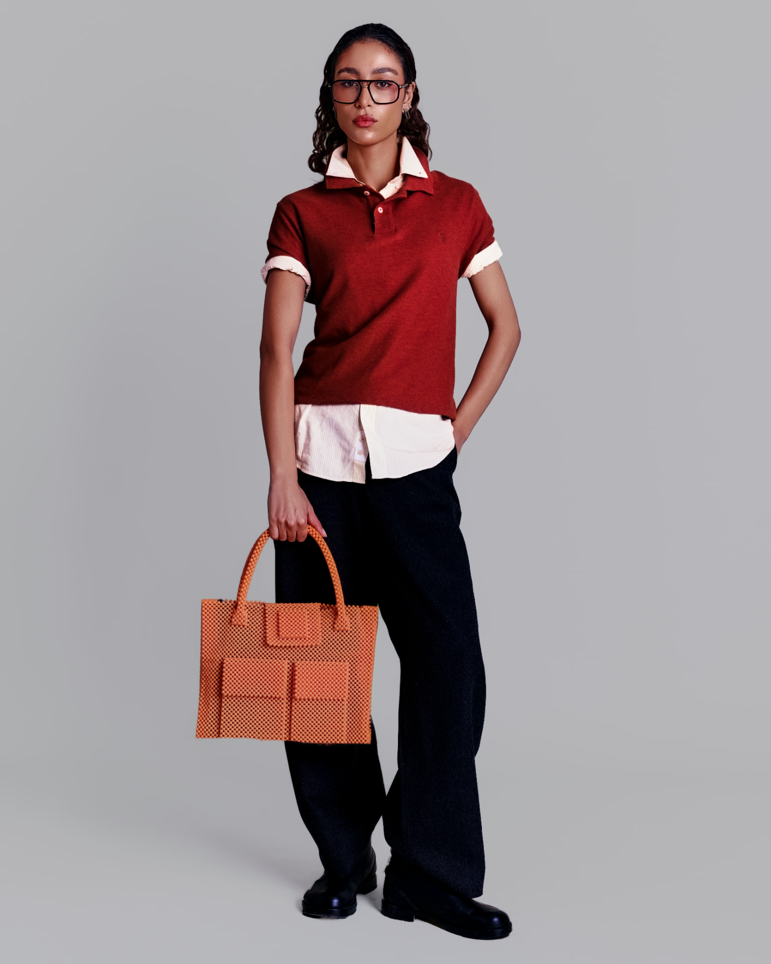 Model in a rust polo holding an apricot beaded tote